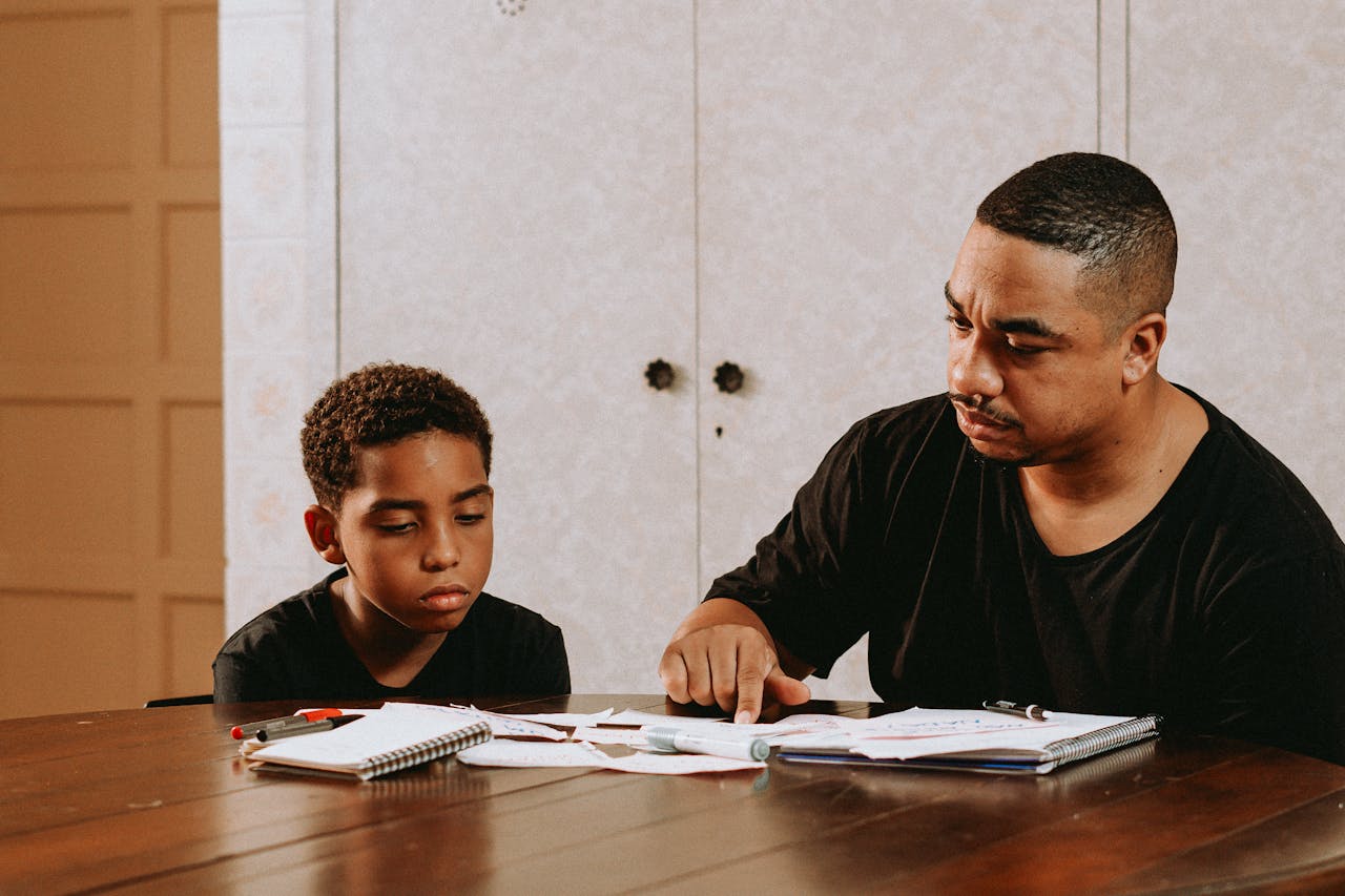 A father helps his son with homework at a dining table, promoting learning and bonding.